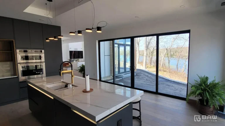Modern kitchen with dark cabinets and a large island in the middle and sliding glass doors overlooking the lake